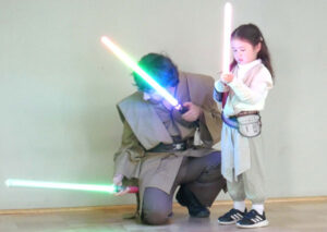Father and daughter in Star Wars costume inspect lightsabers